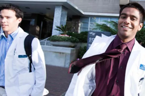 Two UCSF learners in white coats leaving the School of Pharmacy building on the Parnassus campus