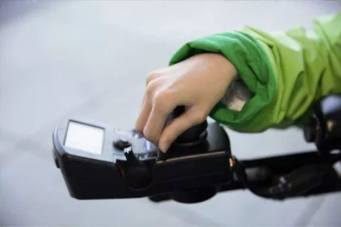UCSF community member's hand placed on the electronic control panel mounted on the end of the armrest of her motorized wheelchair. 