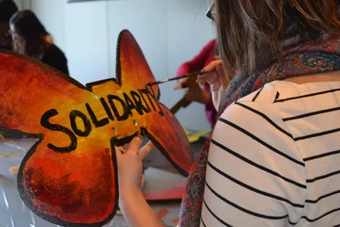 UCSF community member painting 'Solidarity' on butterfly shaped poster, itself painted in monarch butterfly colors